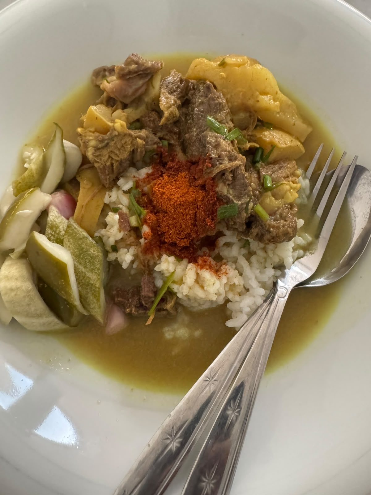 Semangkuk nasi dengan kuah empal gentong, potongan daging, cabai, dan pelengkap.